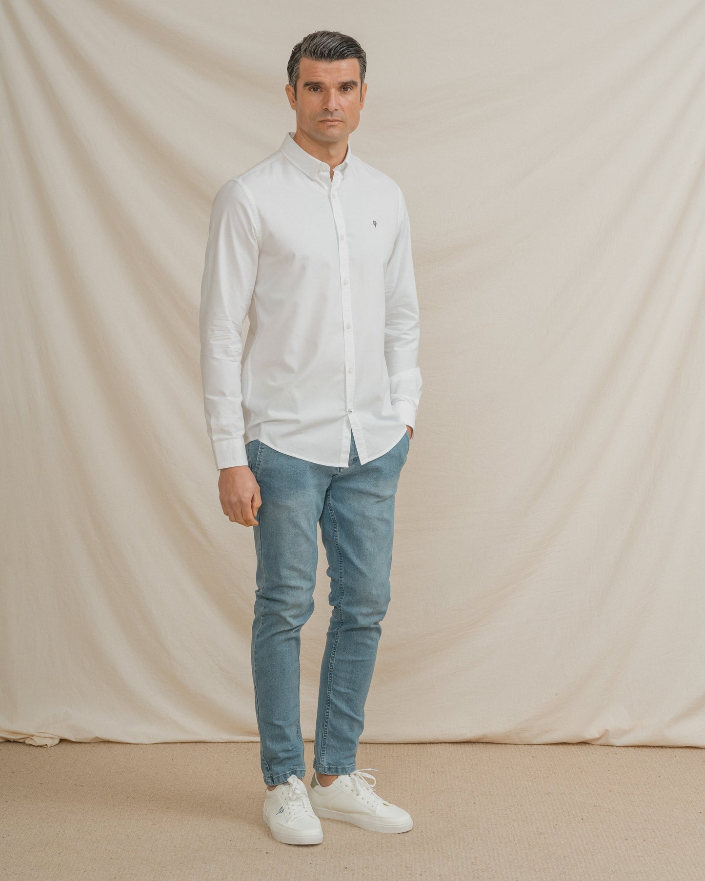 Camisa Oxford blanca de hombre con cuello botonado y detalle de logo en el pecho.