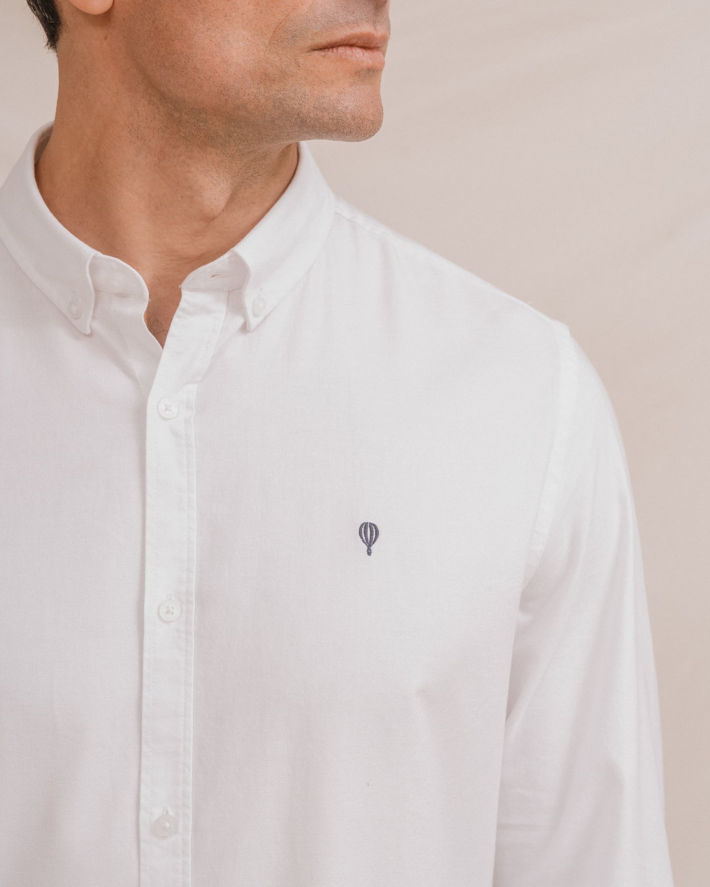 Camisa Oxford blanca de hombre con cuello botonado y detalle de logo en el pecho.