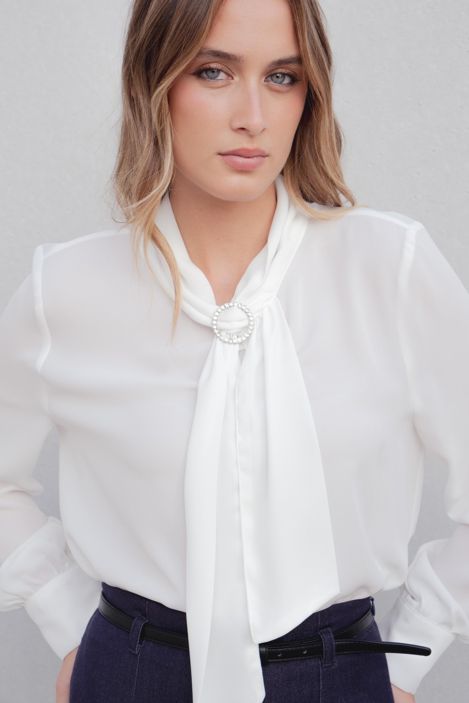 Blusa de manga larga en color (especificar color) con lazada o corbata en el cuello.