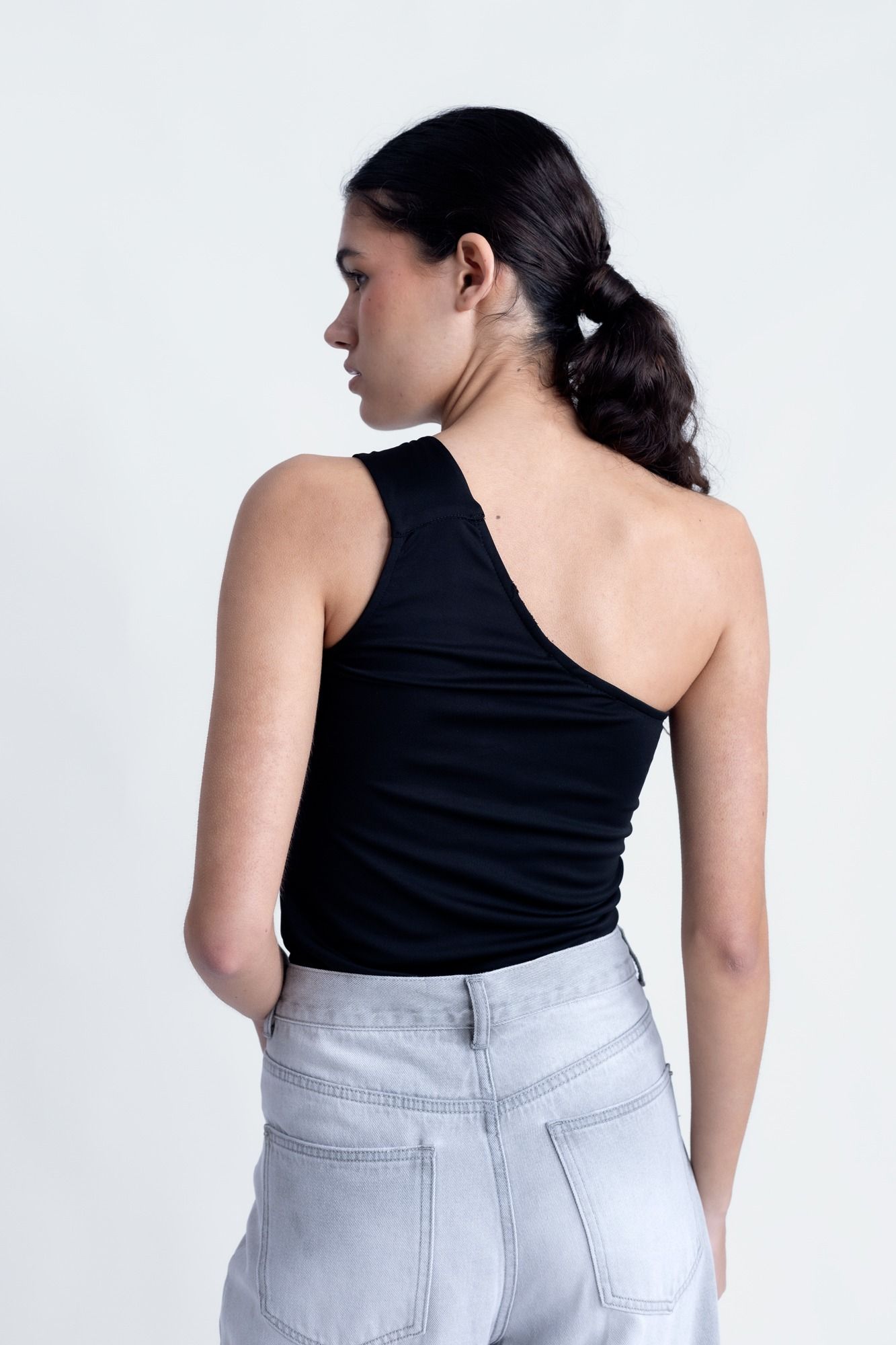 Top corto elástico para mujer en color negro con escote asimétrico de un solo hombro para looks de noche.